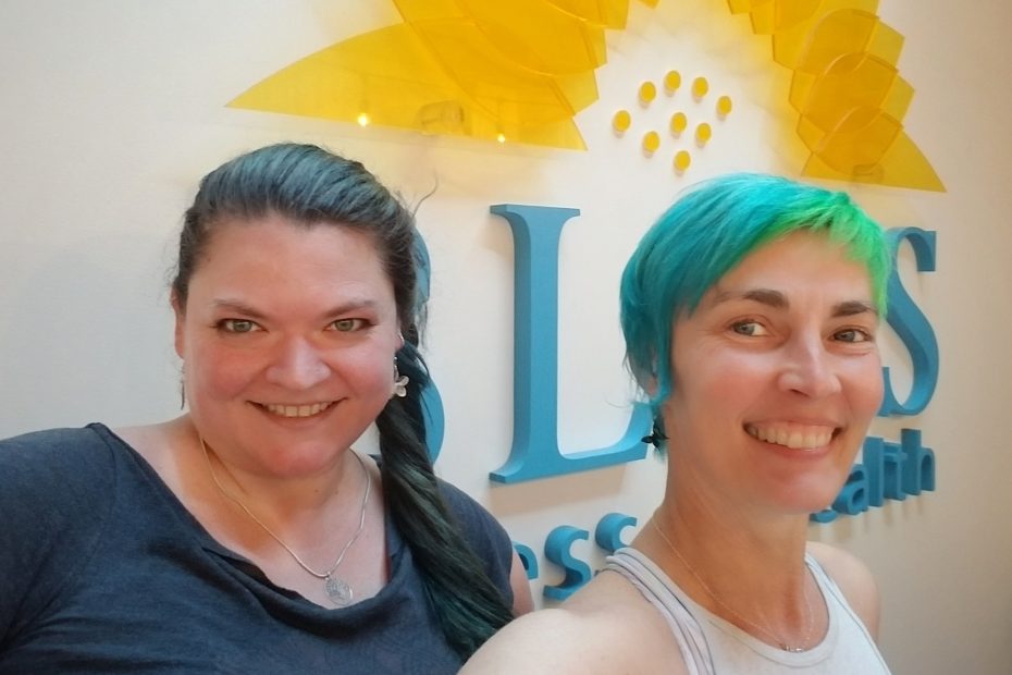 Amy and Mona smiling at the front desk in front of the Bliss Fitness logo